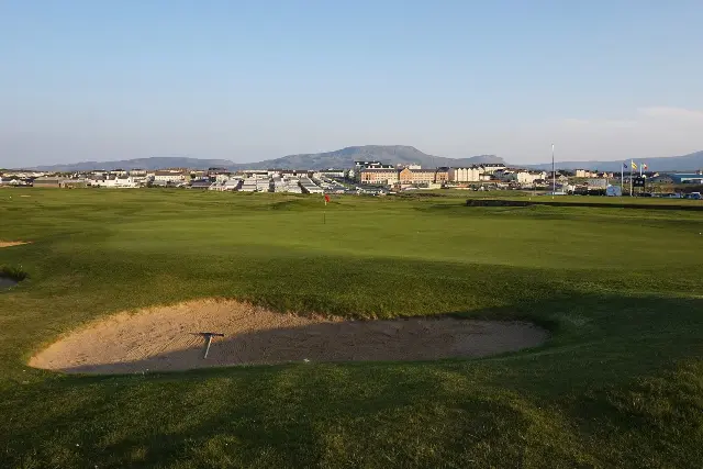 The photograph: a bunker with a rake in it and a flag on the green at Bundoran, the town and a flat-topped mountain behind.