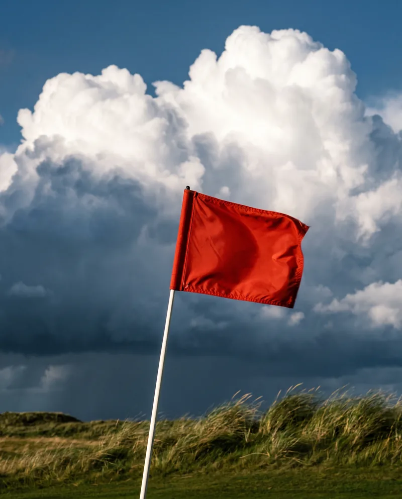 A red flag on its pin against tall cumulus cloud.