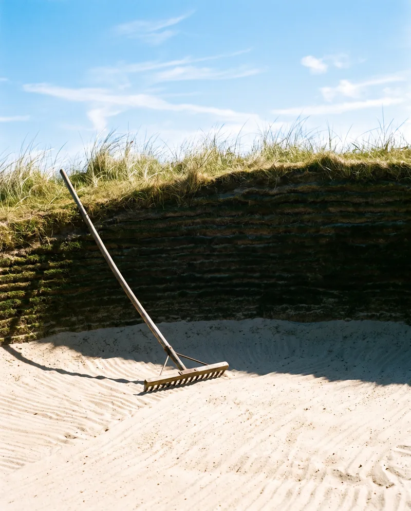A deep pot bunker with a rake lying in the sand.